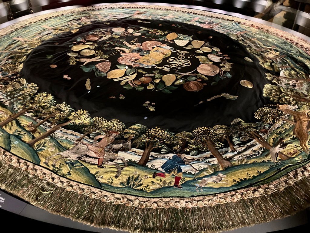 An oval-shaped tablecloth in dark velvet, covered in hand embroidery.