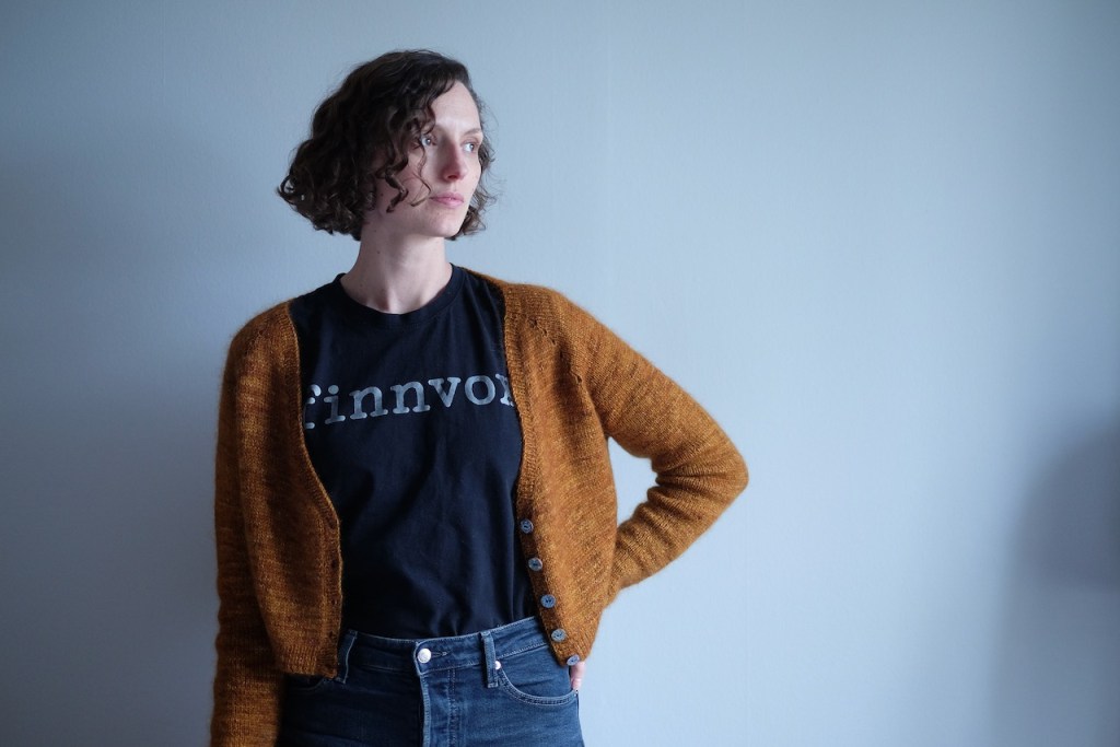 Dianna wears the orangey brown Helix cardigan open over a black T-shirt and jeans.