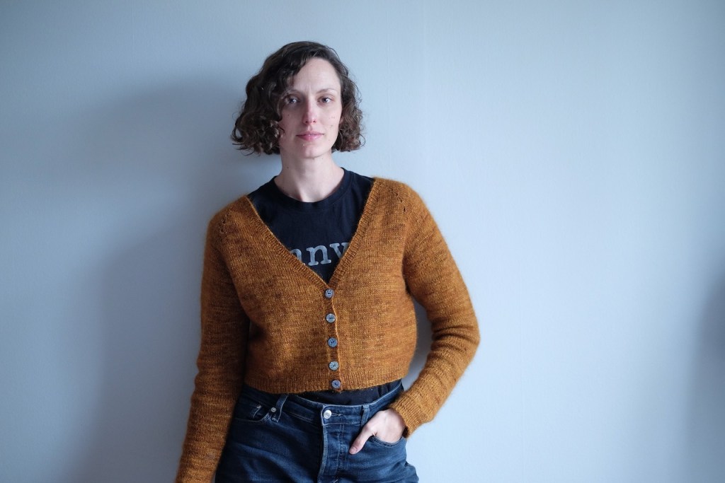 Dianna wears a cropped V-neck cardigan with on hand in her pocket.