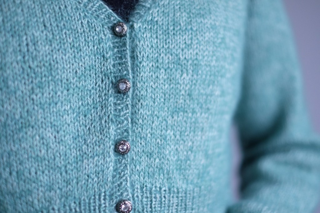 A closeup of the cardigan's buttons, small silver buttons with a rhinestone in the center and swirly details in the silver rim.
