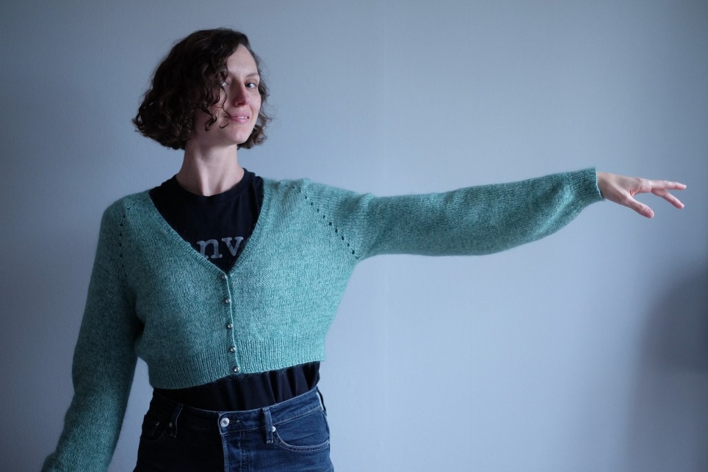 Dianna holds one arm to the side, showing off the slightly billowy bishop sleeve of her minty green cardigan.